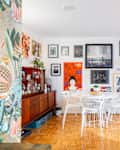 Bright living space featuring a round dining table with white chairs, red accent chairs, and a gallery wall of diverse artwork.