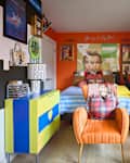 Colorful bedroom featuring a striped bedspread, orange armchair with a heart pillow, and eclectic wall art.