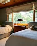 Cozy bedroom with two twin beds, wooden ceiling, green walls, and a window with natural light.