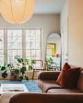 Cozy living room with a fireplace, piano, plants, and a large pendant light, featuring a brown sofa and a coffee table.