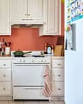 Cozy kitchen with white cabinets, a green pot on the stove, and various kitchen tools displayed on the wall.