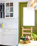 Bright kitchen with white cabinets, colorful striped shelves, a farmhouse sink, and a bowl of vegetables on the table.
