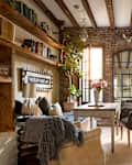 Cozy living space with exposed brick walls, wooden beams, a small table, and a window seat adorned with plants and flowers.