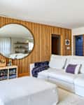 Bright living room featuring a white sectional sofa with decorative pillows, a round mirror, and wooden shelving with decor.