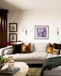 Cozy living room with a light gray sectional sofa, decorative pillows, framed art, and a view of the city through large windows.