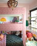 Bunk bed with pink patterned fabric, colorful wall murals, plush toys, and a cozy reading nook in a children's room.