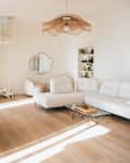 Bright living room featuring a white sectional sofa, wooden sideboard, spiral staircase, and decorative shelves.