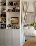 Cozy room with a bed behind curtains, surrounded by bookshelves, a round wooden table, and a floral arrangement.