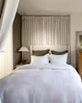 Cozy bedroom featuring a light bedspread, green accent pillows, wooden dresser, and soft curtains.
