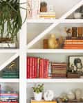 Bookshelf with colorful books, potted plants, small sculptures, and decorative items arranged on white shelves.