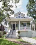Two-story house with front porch, American flag, and lush greenery, featuring a staircase leading to the entrance.