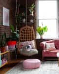 Cozy living room with pink sofa, hanging chair, arcade machine, plants, and fluffy decor.
