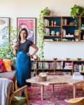 Living room with colorful cushions, wooden shelves, books, plants, and a woman standing near a sofa.