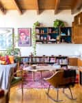 Mid-century modern living room with wooden ceiling, colorful rug, bookshelves, plants, and a rocking chair.