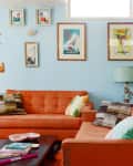 Mid-century living room with orange sofas, vintage clock, blue walls, and eclectic wall art.