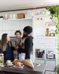Family in modern kitchen with white cabinets, plants, and breakfast items on the counter.
