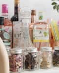 Bar setup with assorted liquor bottles, glass jars of dried herbs, colorful straws, and copper pineapple cups.