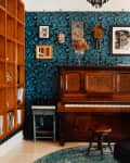 A green and blue floral patterned wallpaper in a living area with a piano