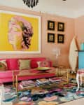 Eclectic living room with pink sofa, colorful rug, yellow artwork, and a turquoise bar table with a patterned chair.