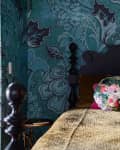 A bed in front of blue floral wallpaper