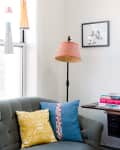 Cozy living room corner with a gray sofa, colorful pillows, floor lamp, and books on a side table.