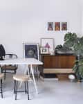 Dining room with white table, eclectic decor, plants, framed art, and a wooden sideboard with a record player.