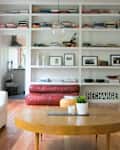 Living room with white sofa, red leather couch, wooden coffee table, and bookshelves filled with books and decor items.