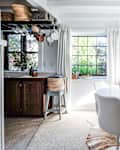 Bright kitchen with white round table, modern chairs, hanging mugs, and large windows with curtains.
