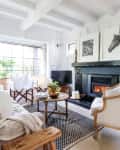 Cozy living room with a fireplace, white armchairs, a sofa with blankets, and framed horse art above the mantel.