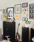 Living room with black shelves holding vinyl records, eclectic wall art, a guitar, and a sofa with a cookie pillow.