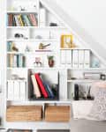 Built-in white shelves with books, decor, and storage boxes beside a gray sofa with patterned pillows.