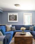 Blue living room with a large sectional sofa, wooden coffee table, and a camera print on the wall.