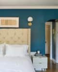 A bed with a tall upholstered headboard and sconces and an art piece above it