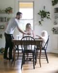Family dining in a plant-filled room with wooden table, black chairs, and bookshelves.