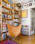 Cozy reading nook with leather chair, colorful rug, bookshelves, framed art, and a bar cart with glassware.