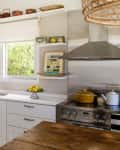 Bright kitchen with white cabinets, open shelves, a window, and a stainless steel stove with a yellow pot.