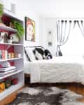 Bright bedroom with white bedding, black and white curtains, a full-length mirror, plants, and a bookshelf with decor.