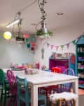 Craft room with colorful chairs, floral wallpaper, pendant lights, and shelves filled with craft supplies and books.