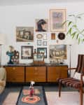 Living room with a mid-century sideboard, eclectic wall art, striped armchair, and large potted plants.