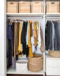 Organized closet with hanging clothes, wicker baskets on top, and woven baskets on the floor.