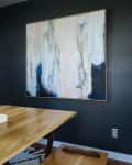 Dining room with wooden table, abstract wall art, gold candlesticks, and pink flowers in a vase.