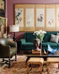 Eclectic living room with green sofa, vintage art, Buddha statue, and floral decor on a patterned rug.
