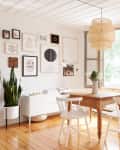 Dining area with wooden table, white chairs, wall art, potted plant, and wicker pendant light near a wooden door.