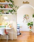 Bedroom with red bed frame, white desk, plants, and archway leading to a room with a blue chair and wall decor.