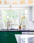 Bright kitchen with green cabinets, black countertop, gold faucet, and a potted orchid by a large window.