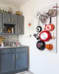 Gray kitchen cabinets, white stove, and pegboard with hanging pots and pans.