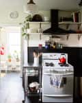 Cozy kitchen with dark cabinets, wooden countertops, open shelves, a red kettle on the stove, and potted plants.
