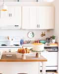 Bright kitchen with white cabinets, cake and pastries on island, and a fridge covered in photos and notes.