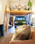 Loft apartment with a vintage van under a wooden mezzanine, pink sofa, and plants.