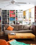 A white bookshelf filled with color-coded books separating a living room and entryway